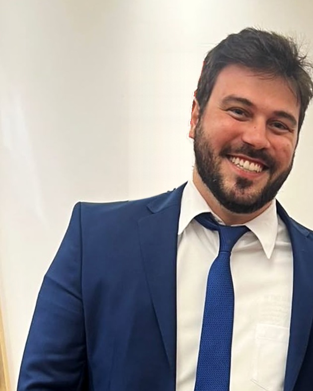 Caio Regagnin sorrindo, de terno e gravata azuis